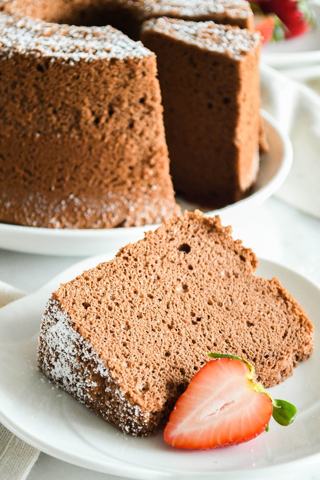 A slice of cotton-soft chocolate chiffon cake on a tea plate with a slice of strawberry.